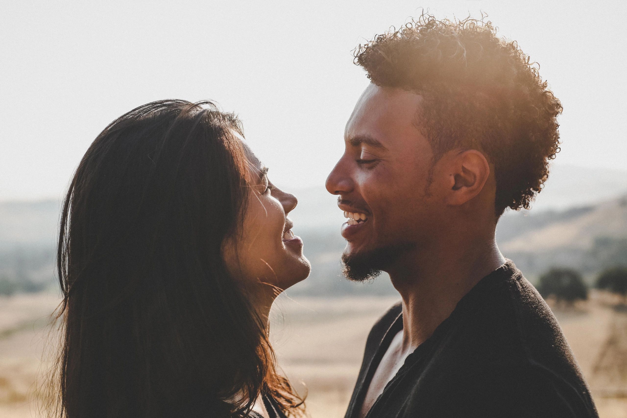  A smiling man and woman, both with curly hair, stand closely, looking at each other.